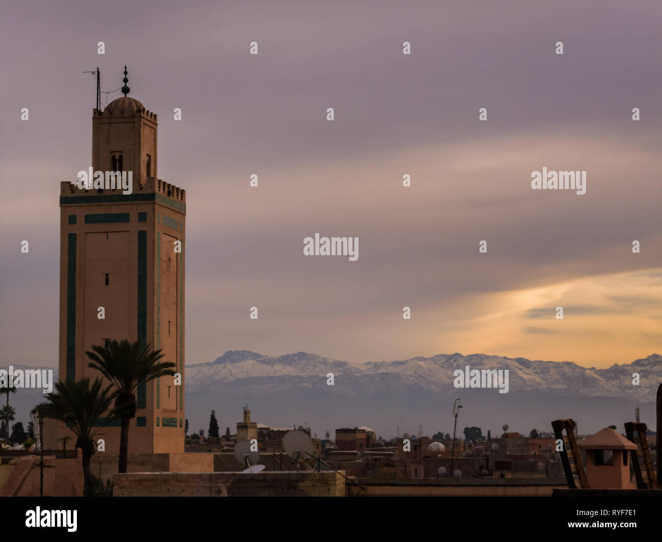 I soli raggi schiariscono brevemente sulle montagne innevate dietro il minareto di Marrakech Foto Stock