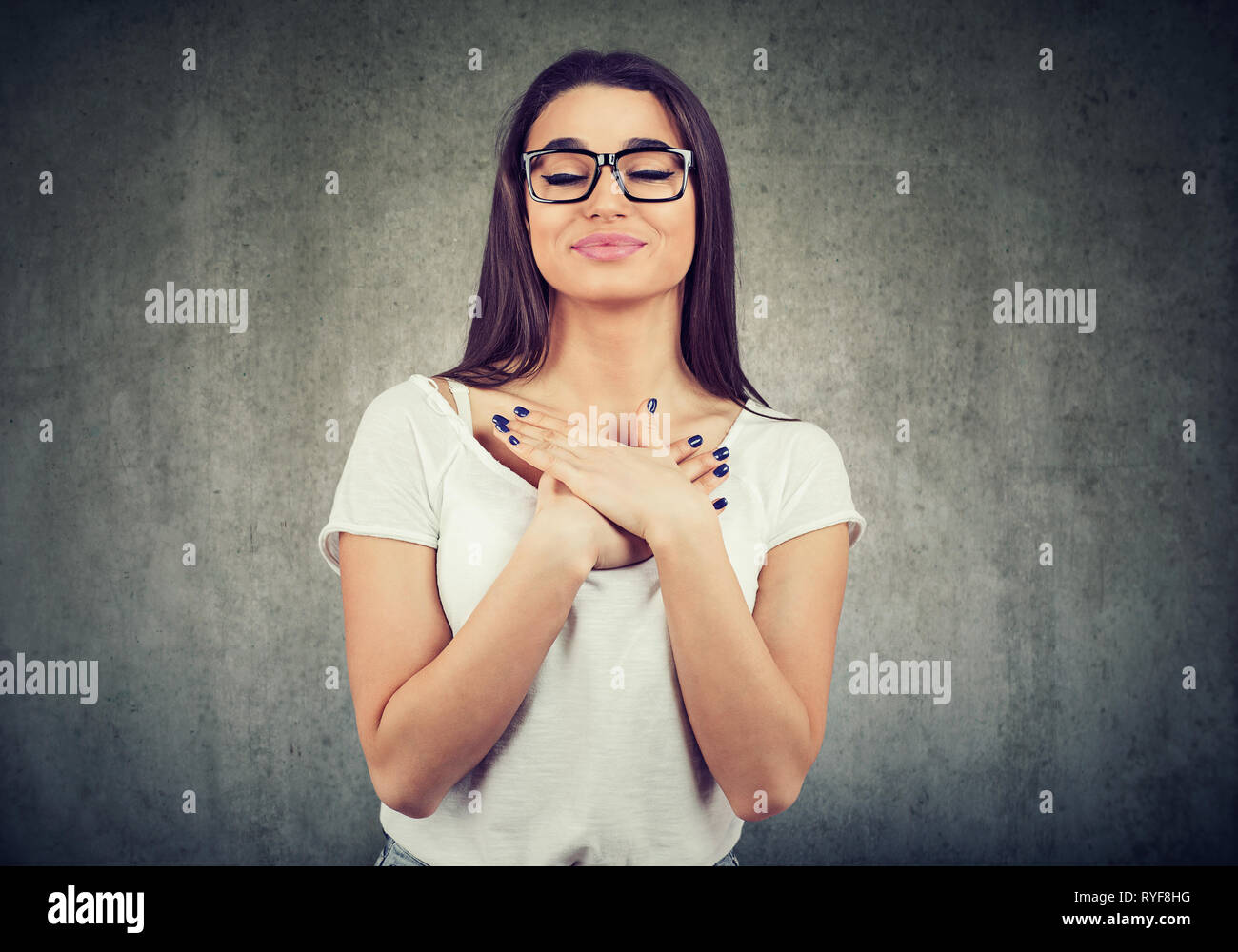 Donna con gli occhi chiusi tiene le mani sul petto vicino al cuore, mostra la gentilezza, esprime sincere emozioni, essendo natura generosa. Il linguaggio del corpo sentimenti concept Foto Stock