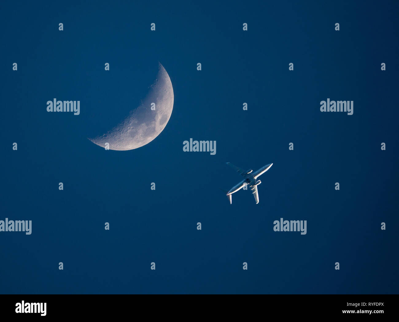 Un basso-volo aereo commerciale passa da una falce di luna in un cielo blu scuro al tramonto. Foto Stock