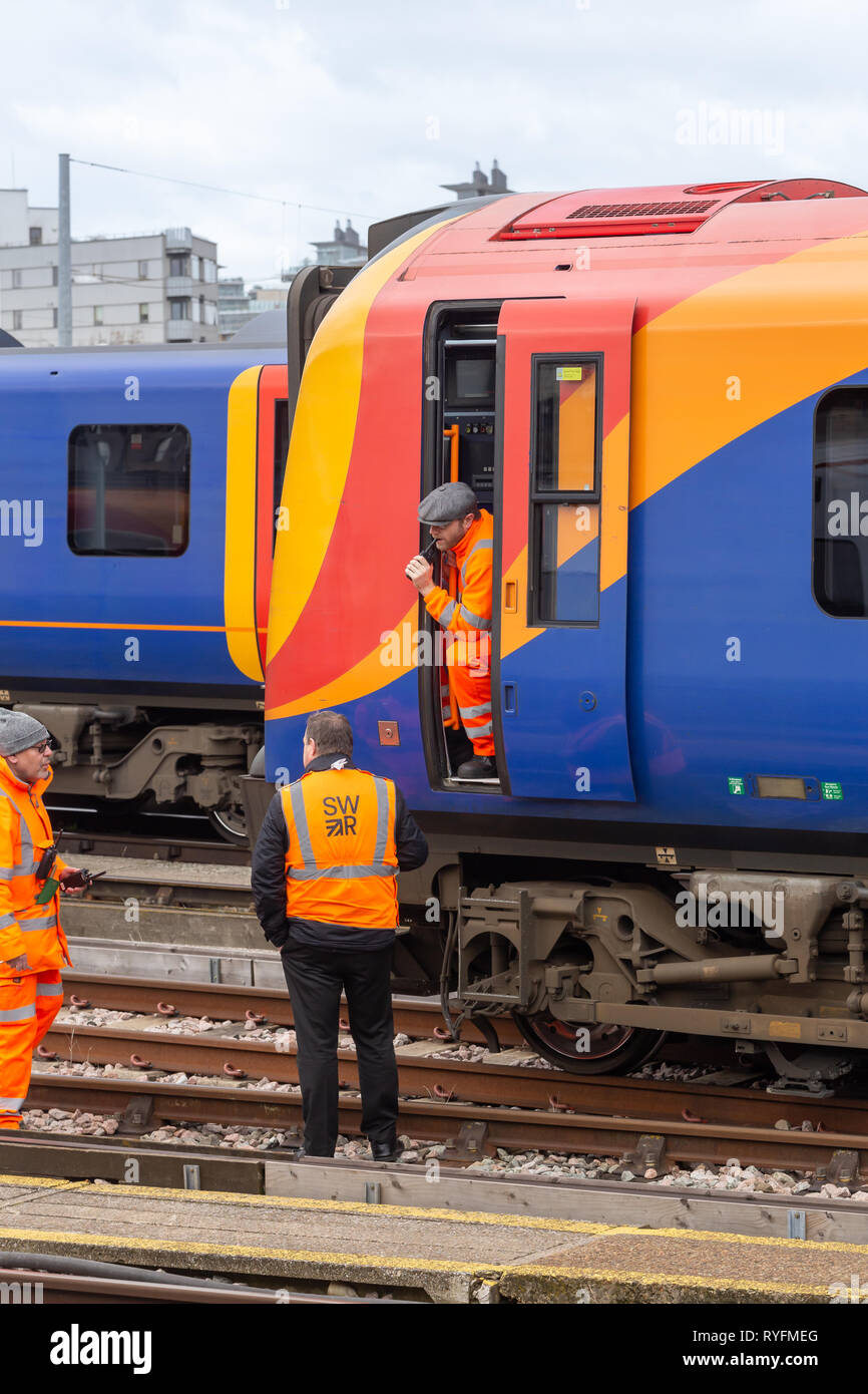 Clapham Junction, Londra, Regno Unito; 13 marzo 2019; Macchinista si appoggia al di fuori della cabina. Colloqui con due colleghi. Tutti arancione di usura ad alta visibilità indumenti di sicurezza Foto Stock