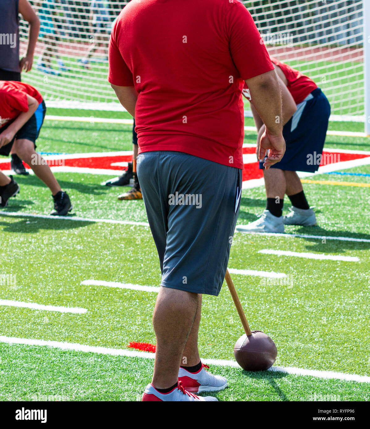 Un allenatore di calcio ha un campo di calcio attaccato ad un bastone per addestrare il lineman difensivo del tempo di reazione durante l'estate pratica su un campo di tappeto erboso. Foto Stock