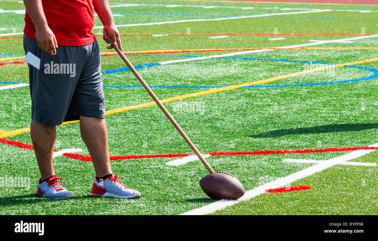 Un allenatore di calcio è su un tappeto erboso verde campo tenendo un calcio sul terreno che è attaccato a un memory stick durante l'estate pratica di preseason. Foto Stock