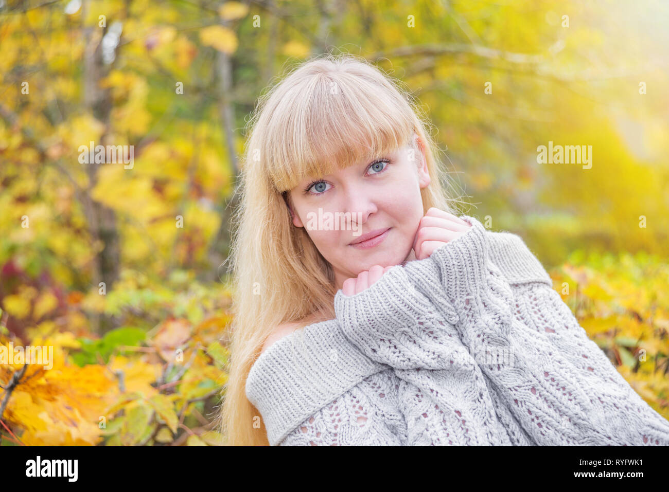 Giovane romantico blue-eyed ragazza bionda con i capelli lunghi e frangia, in un caldo grigio felpa lavorata a maglia, guarda la telecamera in autunno la natura Foto Stock