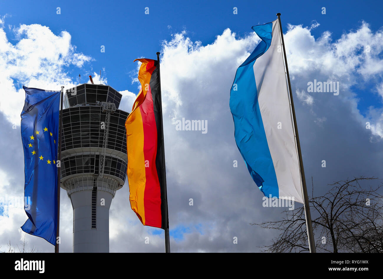 Aeroporto di Monaco di Baviera, Germania - 13 Marzo 2019: bandiera UE, bandiera della Germania e il Land della Baviera bandiera di stato. Sullo sfondo del controllo del traffico aereo a torre. Foto Stock