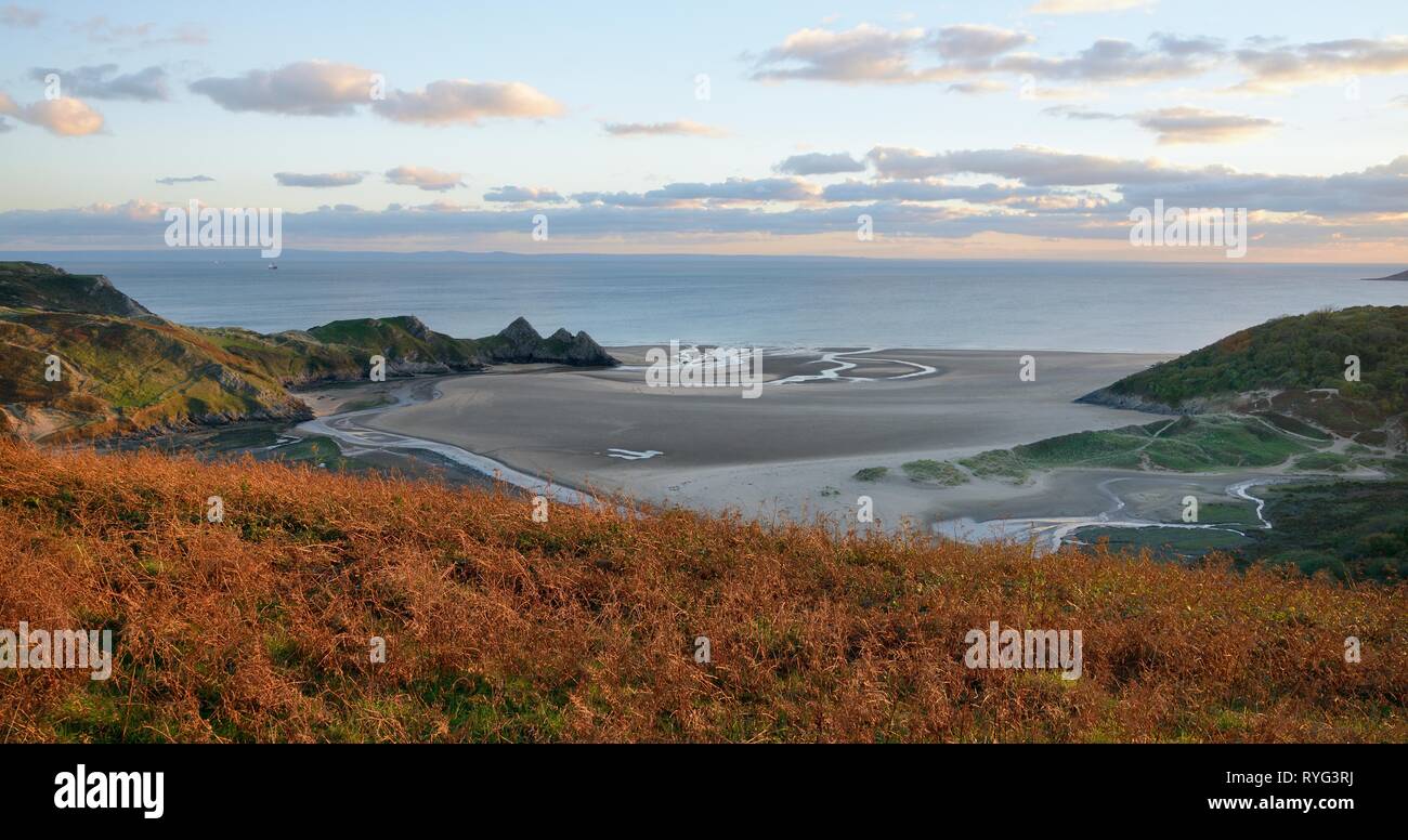 Panoramica di Three Cliffs Bay al crepuscolo con Pennard pillola sinuosità del flusso attraverso la spiaggia al mare, Penmaen, Il Gower, Wales, Regno Unito, ottobre. Foto Stock