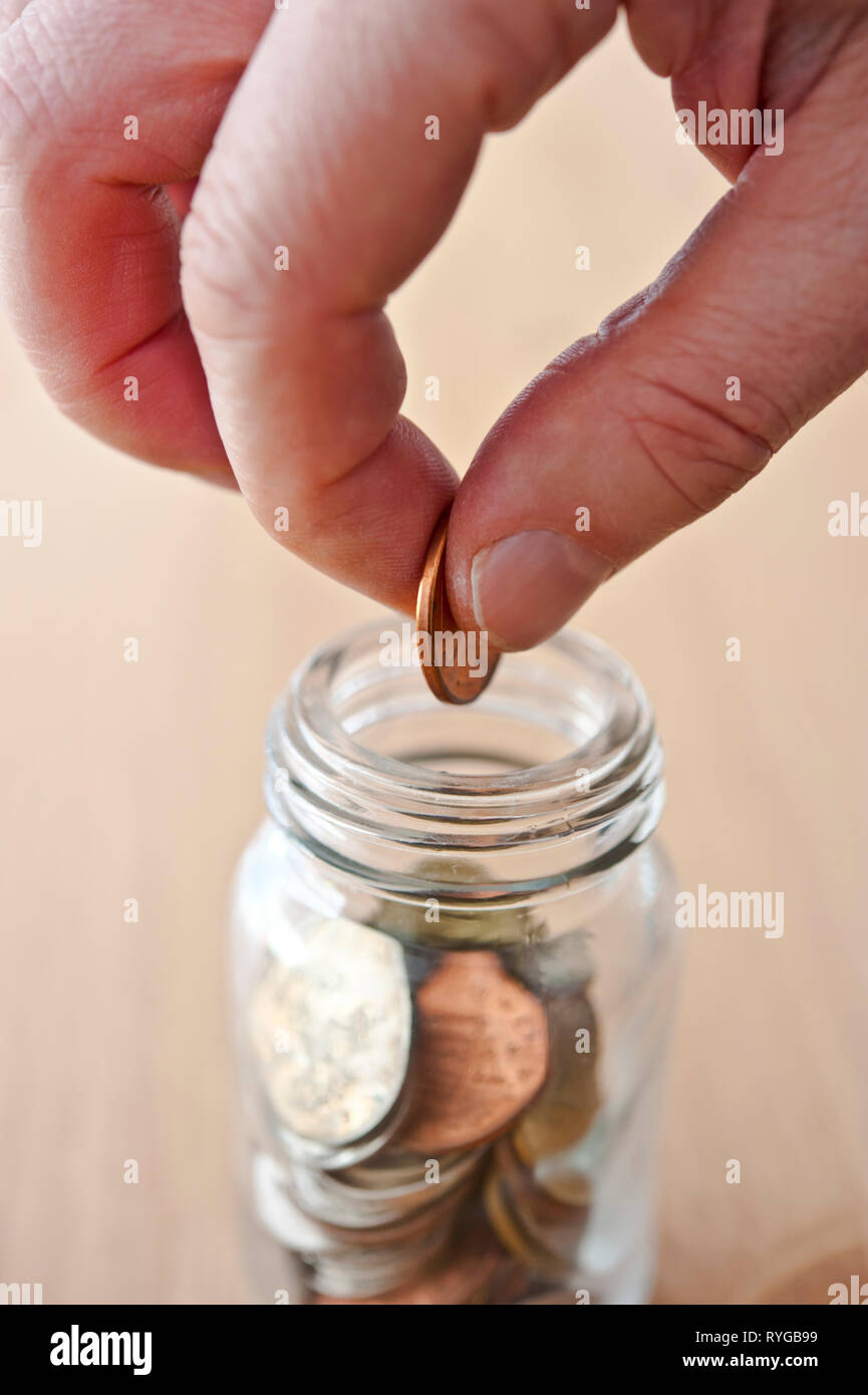 La mano di mettere una moneta in un barattolo di risparmio Foto Stock