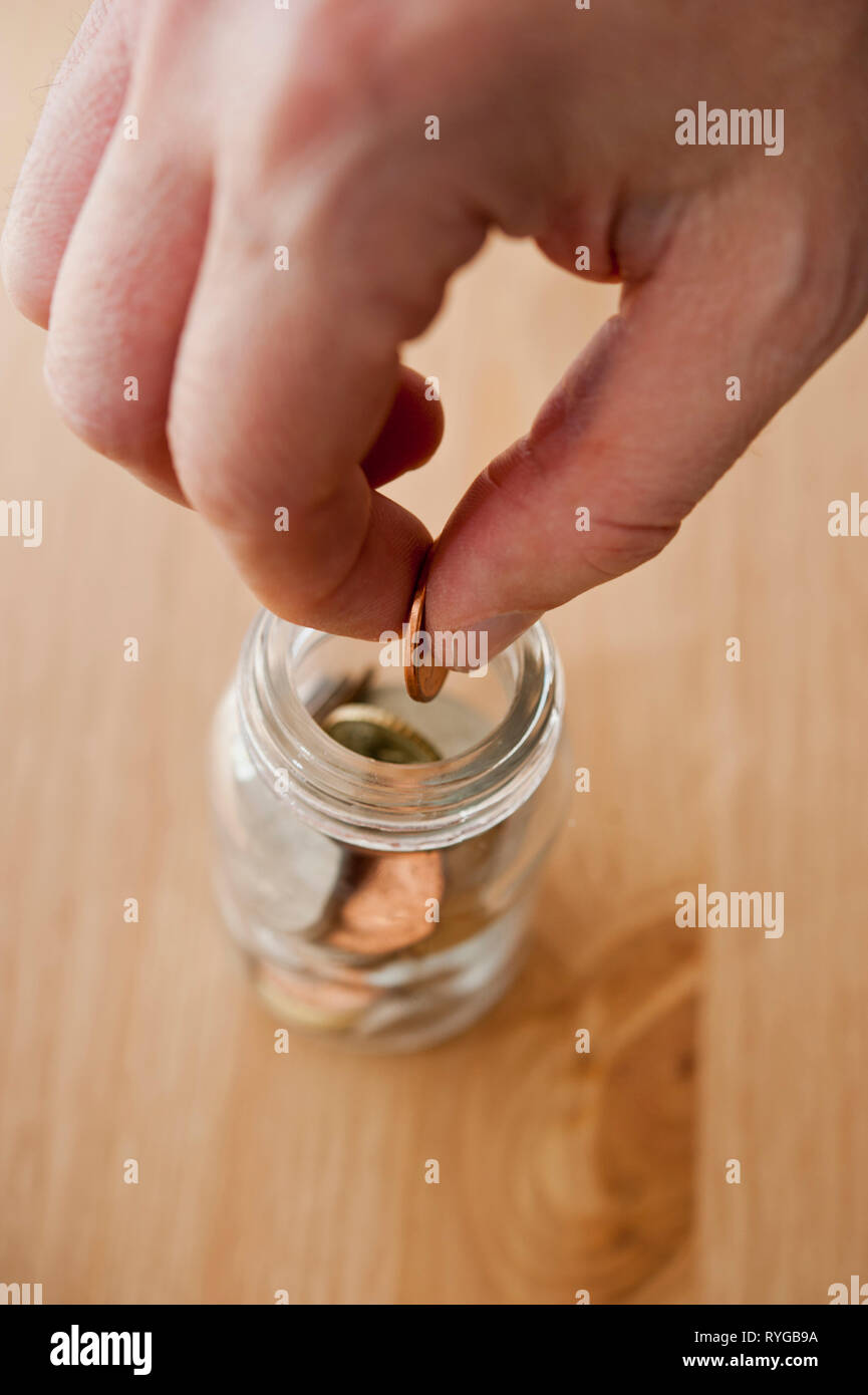 La mano di mettere una moneta in un barattolo di risparmio Foto Stock