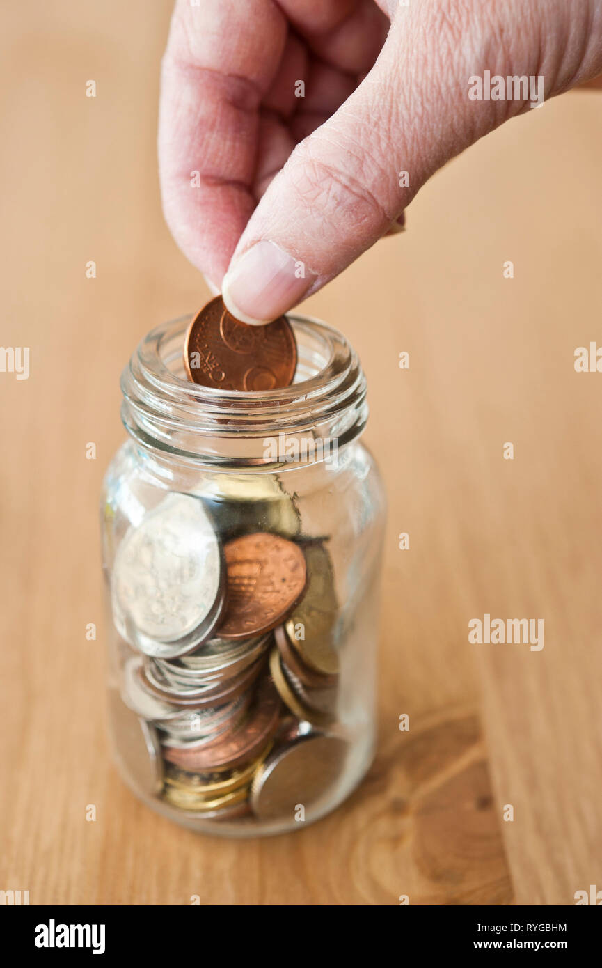 La mano di mettere una moneta in un barattolo di risparmio Foto Stock