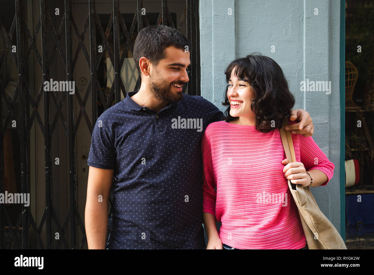Felice e attraente coppia giovane guardando ogni altra sorridente in strada contro uno sfondo di negozi Foto Stock