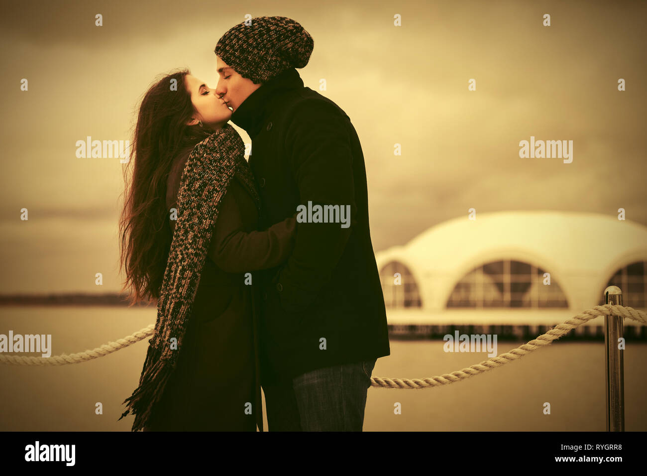 Felice coppia giovane in amore kissing outdoor elegante l uomo e la donna nel classico cappotti beanie e sciarpa Foto Stock