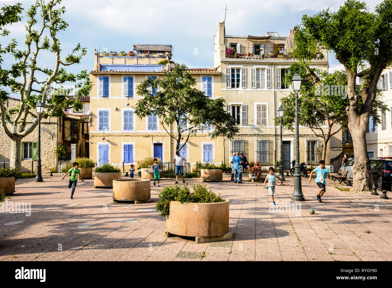 I bambini giocano a calcio tra fioriere nel cuore del quartiere storico di Le Panier a Marsiglia, Francia, mentre anziani chat assieme. Foto Stock