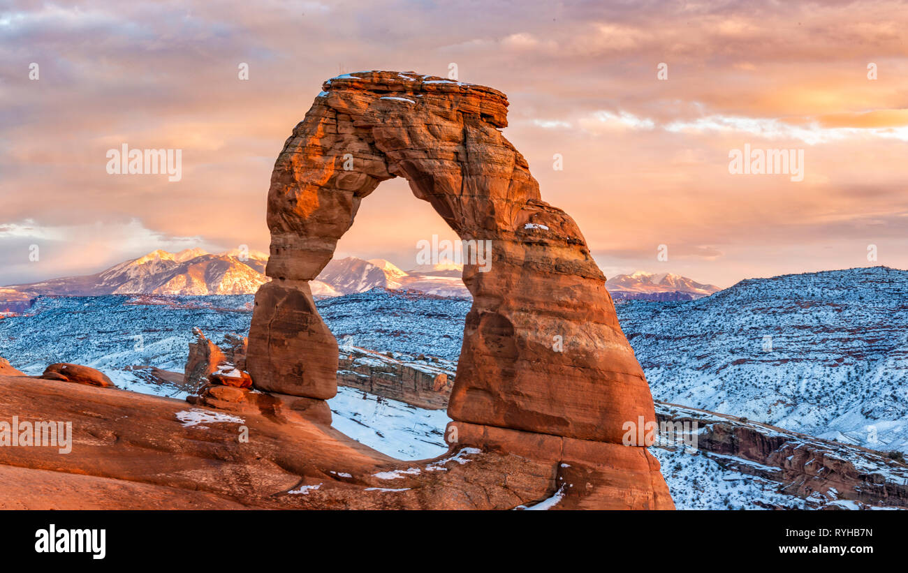 Un tramonto colorato illumina La Sal Mountains dietro iconico Delicate Arch nel dopo un Febbraio 2019 tempesta di neve nel Parco Nazionale di Arches, Moab, Utah. Foto Stock