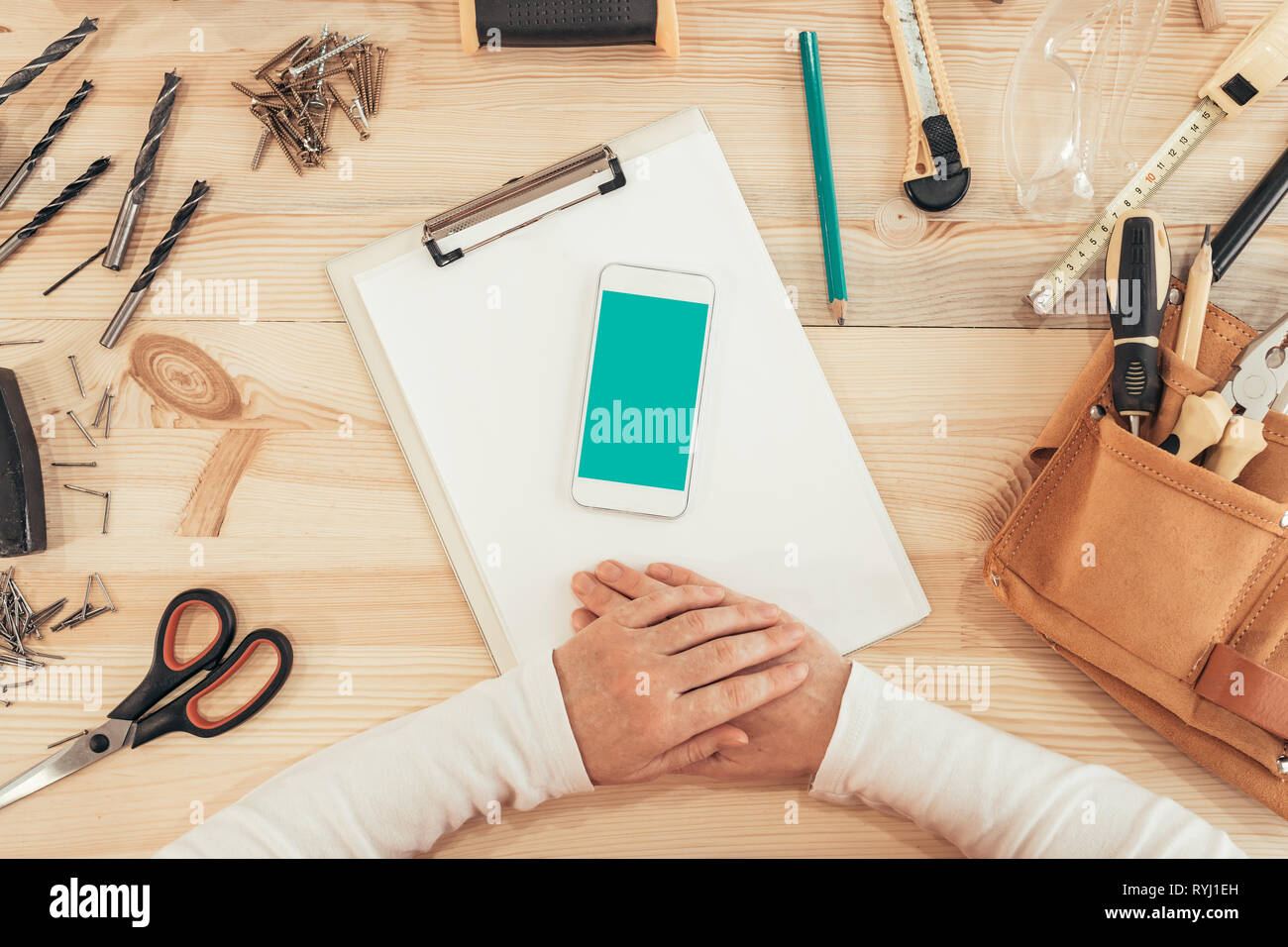 Falegname femmina utilizza lo smartphone, mock up schermo vista dall'alto del legno laboratorio di falegnameria scrivania Foto Stock