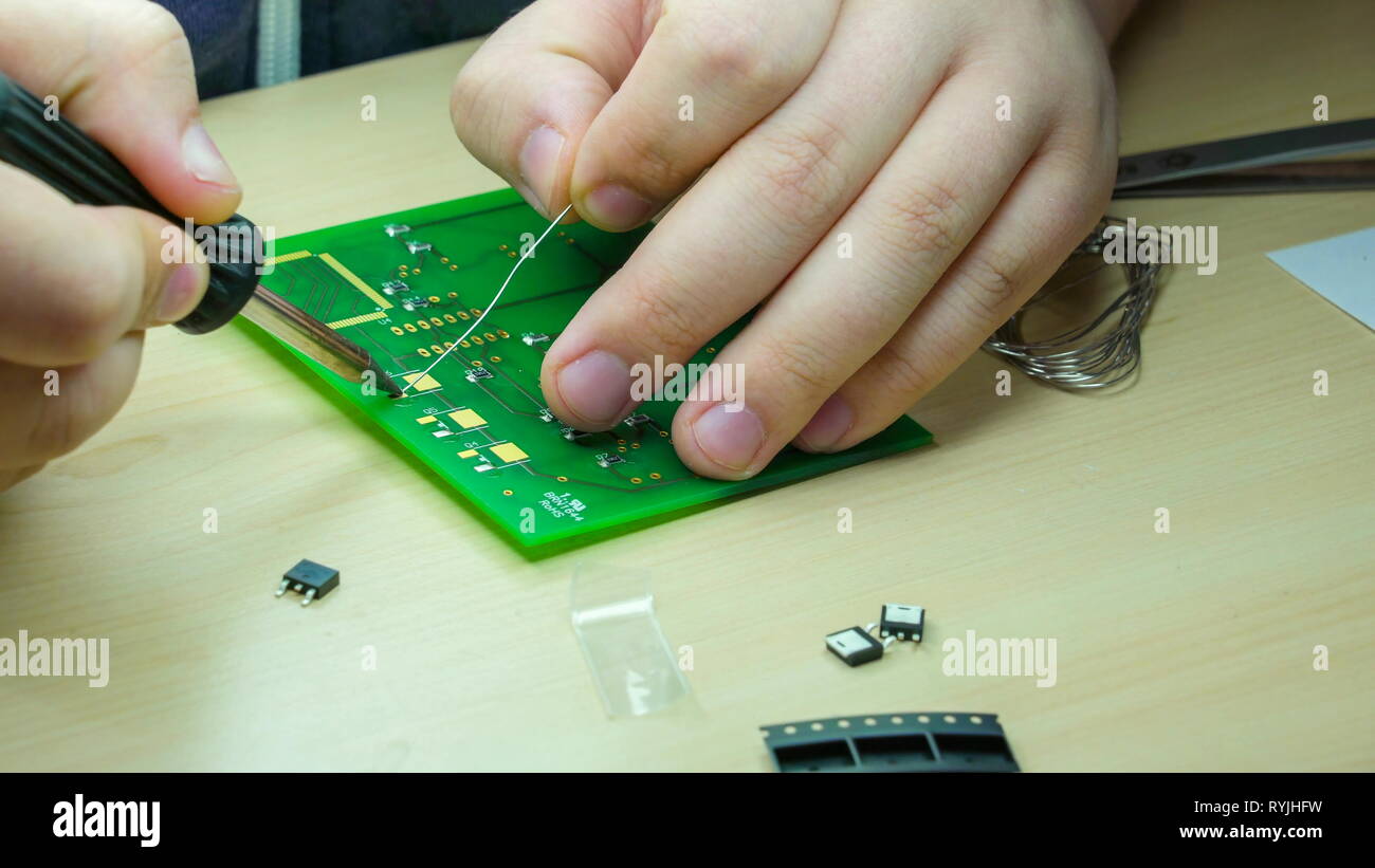 L'occhiata della scheda di circuiti verde con i fili che vengono sciolte con saldatore Foto Stock
