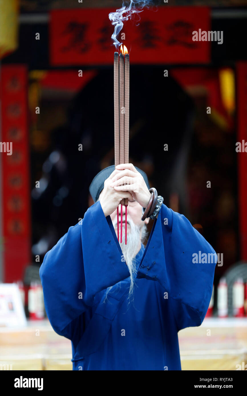 Taoista di missione. Vecchio sacerdote orante con 3 bastoncini di incenso. Singapore. Foto Stock