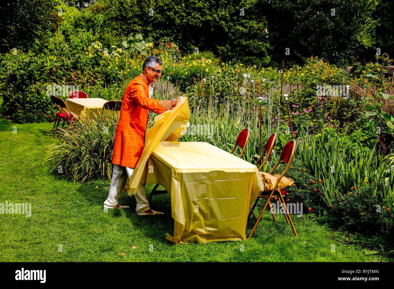 Volontario che stabilisce una tavola per gli ospiti nel giardino fiorito a Bhaktivedanta manor durante Janmashtami festival indù, Watford, Regno Unito Foto Stock