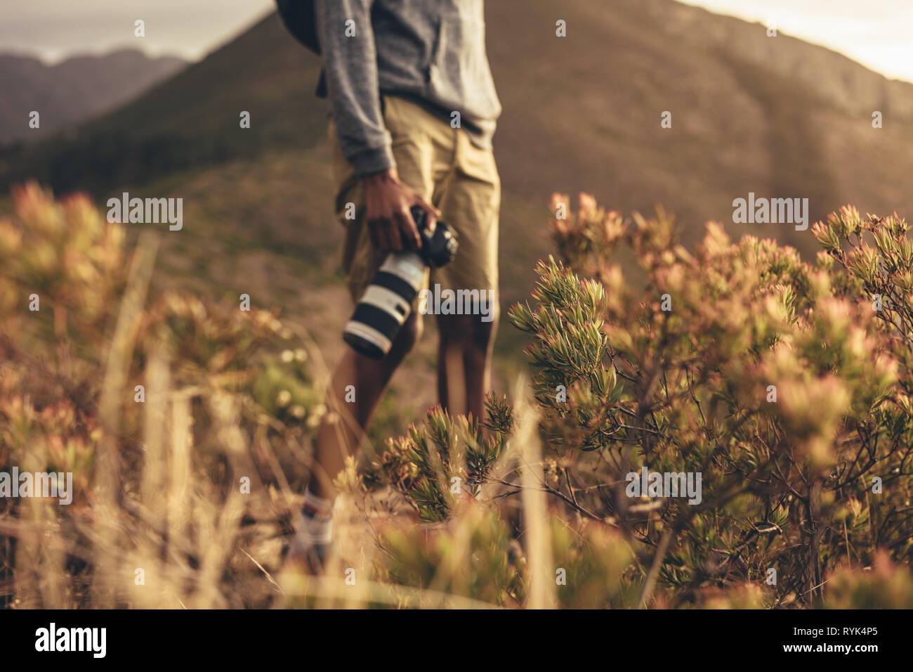 La sezione centrale colpo di uomo in piedi sul sentiero di montagna con la sua fotocamera reflex digitale. Focus su piante selvatiche sul sentiero di montagna con un fotografo in piedi in backgr Foto Stock