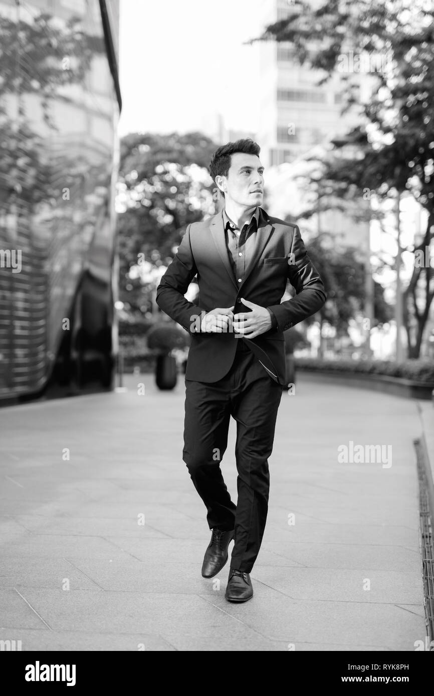 Giovane imprenditore ispanica di pensiero e di camminare al di fuori della costruzione di ufficio in bianco e nero Foto Stock