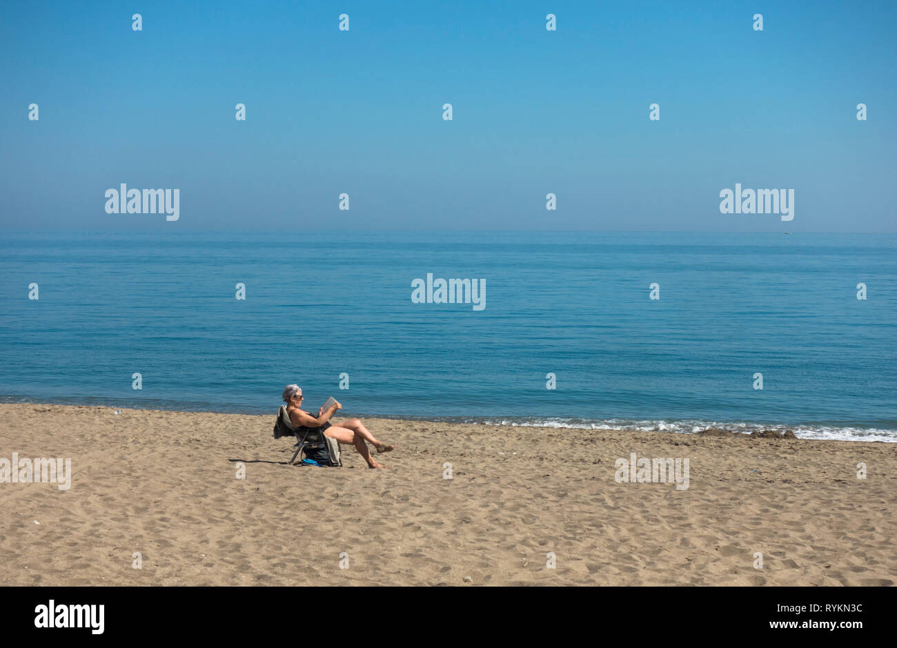 Donna sola sulla spiaggia che legge un libro, Spagna. Foto Stock