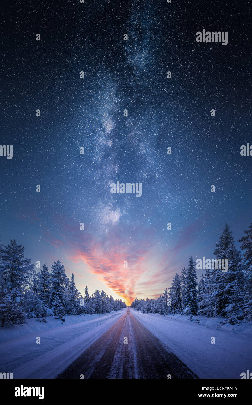 Strada che conduce verso il coloratissimo sunrise tra coperta di neve alberi con epic via lattea nel cielo Foto Stock
