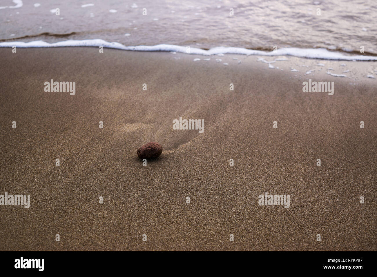 Un lone stone su una spiaggia sul mare con onde sulla riva del mare Foto Stock