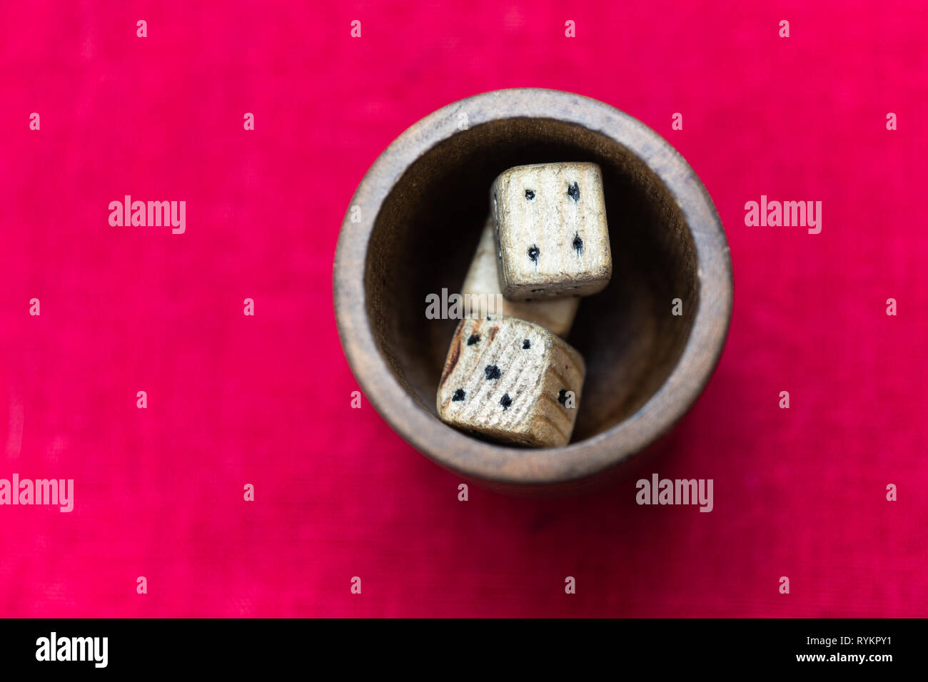 Vintage dadi di legno in una coppa di legno o pentola che sorge su di un soleggiato tavolo ricoperto liscio con panno rosso Foto Stock
