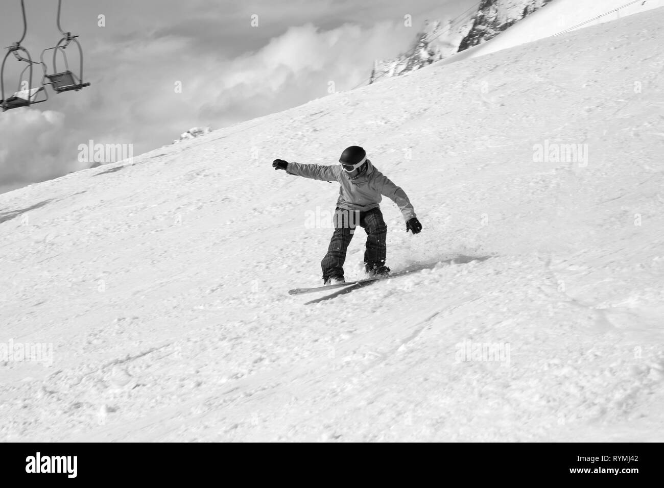 Snowboarder jumping sulla neve sulle piste da sci, vecchia seggiovia e clody sky a sfondo. Montagne del Caucaso nella soleggiata giornata invernale, regione Dombay. Nero e w Foto Stock