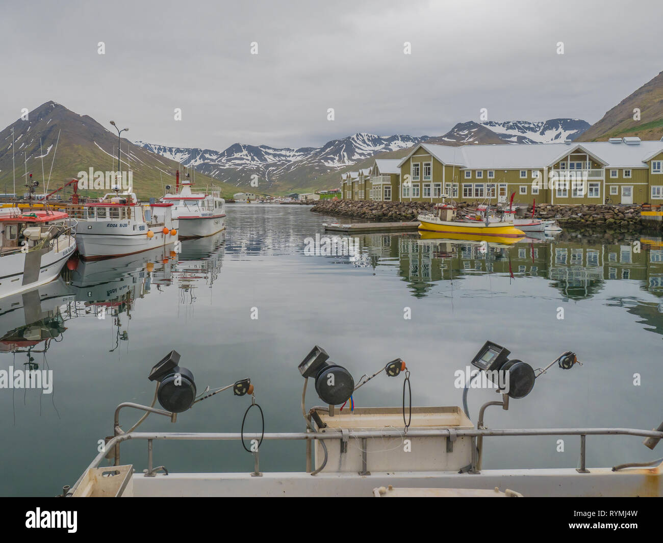 Barche da pesca lungo il porto ancora al di fuori del Siglo Hotel con le montagne che si innalzano per oltre la città di Siglufjörður (Siglufjörður Affitto) Islanda Foto Stock