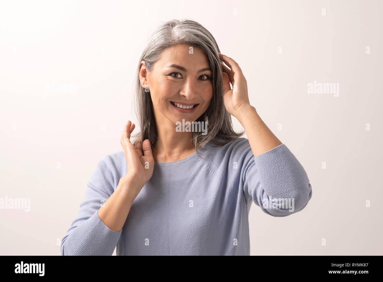 Sorridente donna asiatica tocca i suoi capelli grigi Foto Stock