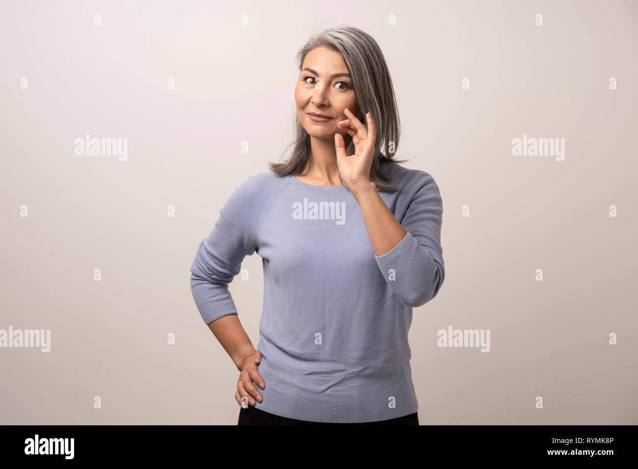 Sorridente donna asiatica tocca i suoi capelli grigi Foto Stock
