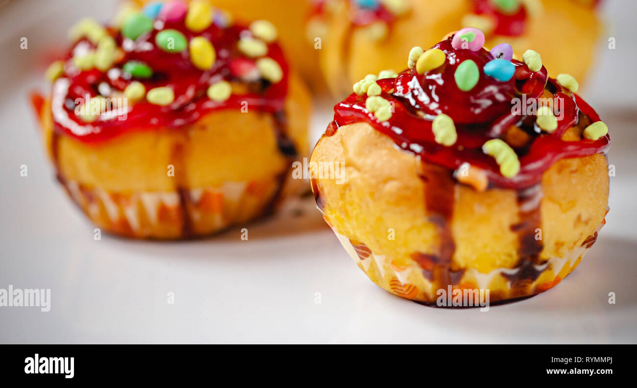 Close-up di guarnito muffin con condimenti di caramella dolce gelatina e scuro di sciroppo al cioccolato bianco nel vassoio. Foto Stock