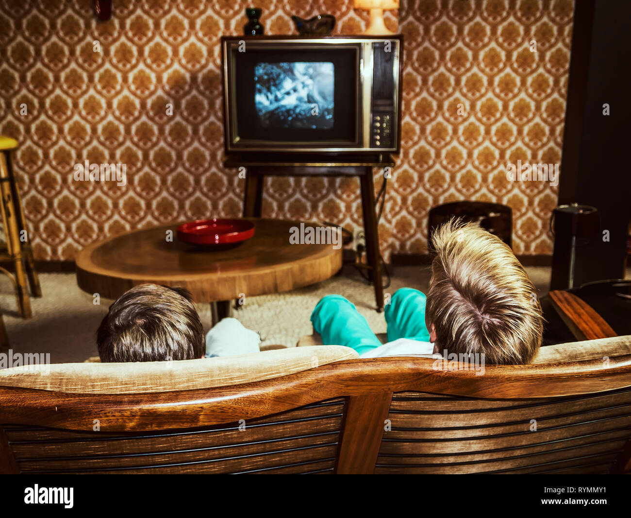 Due ragazzi guardano la televisione a casa in stile anni '50, inquadratura da dietro Foto Stock