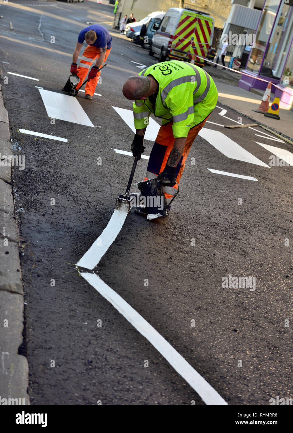 Workman applicando hot strada bianca Vernice per marcatura a linea su zebra-striscia pedonale e attraversare a piedi sulla nuova strada asfaltata Foto Stock