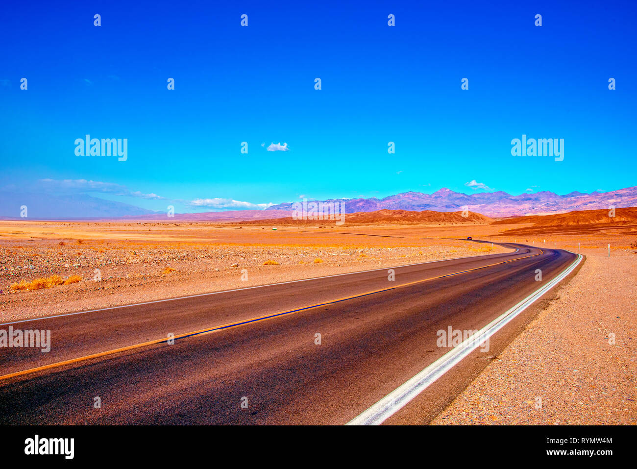 Deserto autostrada che conduce attraverso il deserto arido verso montagne brulle al di là. Foto Stock