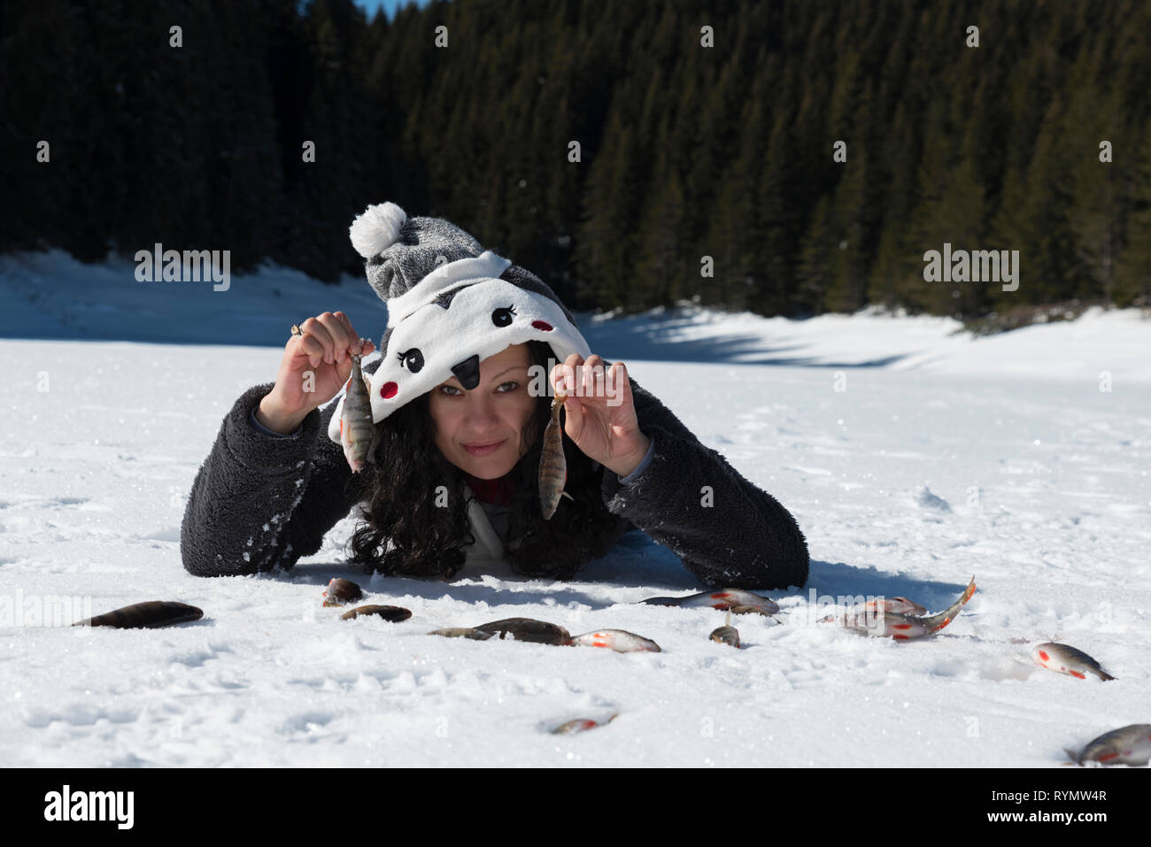 Donna in costume di un pinguino tenendo il pesce e posa su una neve su un lago ghiacciato in montagna durante la stagione invernale il fuoco selettivo Foto Stock