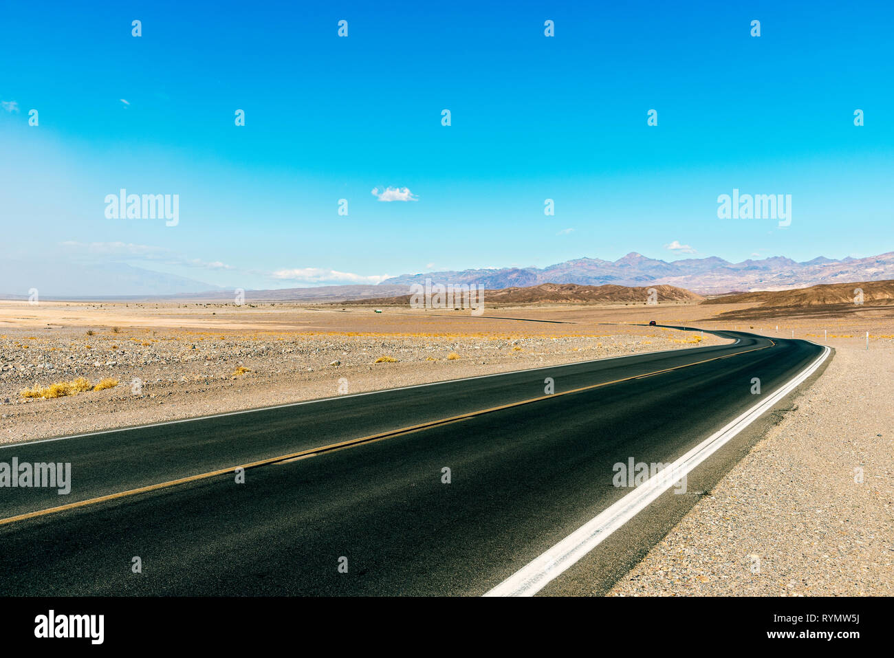 Deserto autostrada che conduce attraverso la terra sterile sotto il cielo blu. Foto Stock