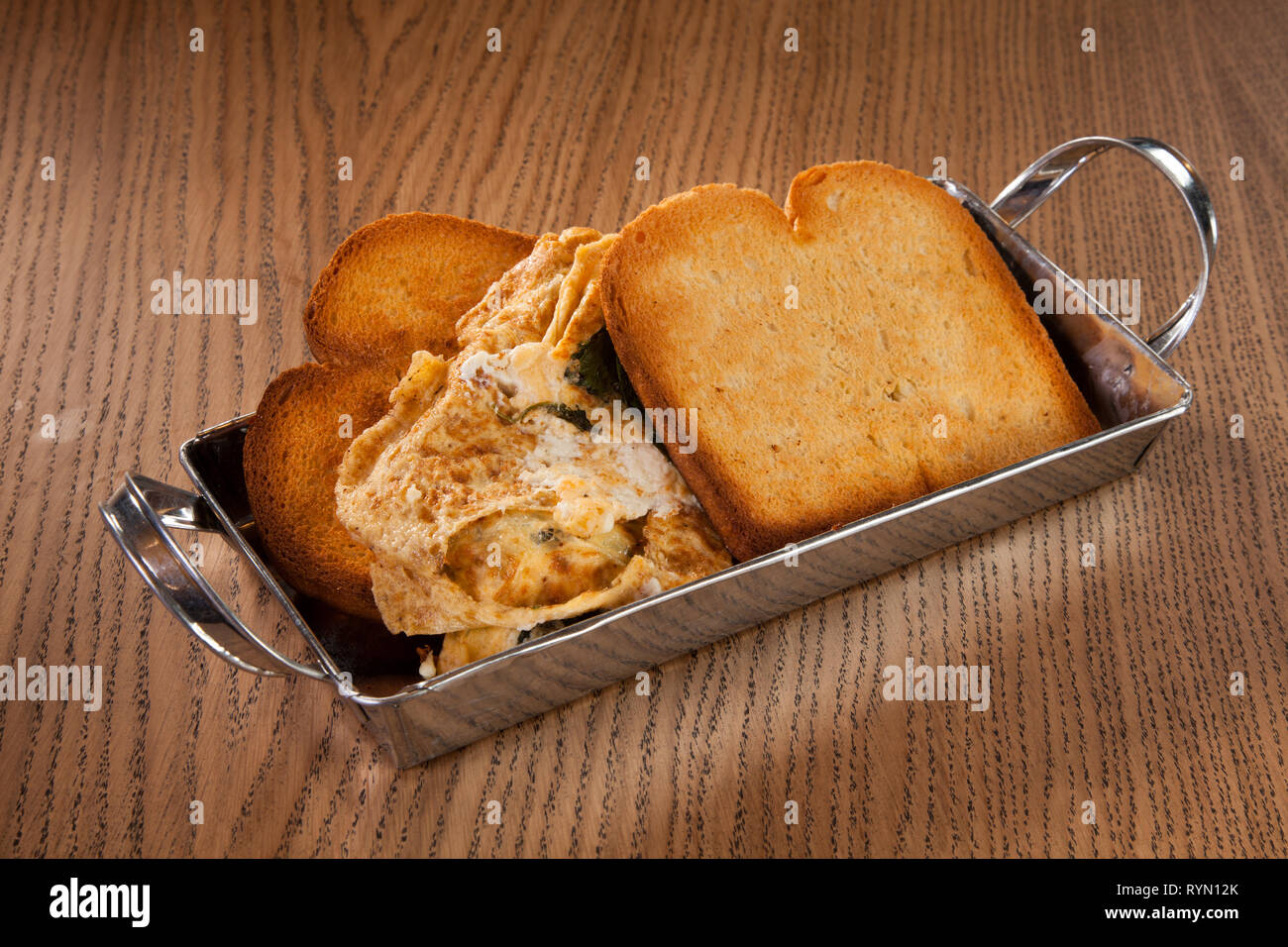 Fette di pane tostato con formaggio tagliati e uova strapazzate nel piatto di alluminio sul tavolo di legno per la colazione o un pasto leggero Foto Stock
