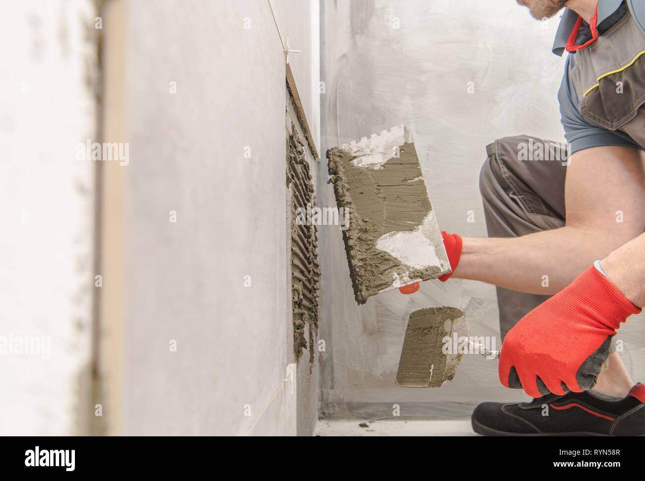 Lavoratore Moderno Installazione di piastrelle in ceramica. Piastrella caucasica Installer sul lavoro. Bagno rimodellamento osseo. Foto Stock