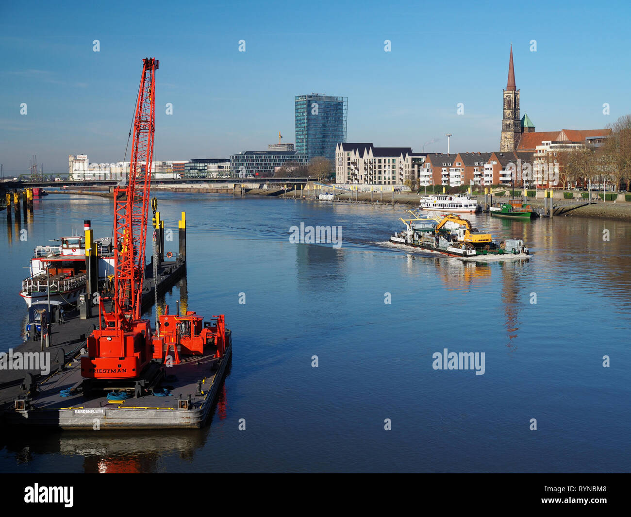 Bremen, Germania - Febbraio 14th, 2019 - Pier con diverse navi di piccole dimensioni e di colore rosso brillante gru galleggiante, chiatta con draghe e dello skyline della città con Weser Foto Stock