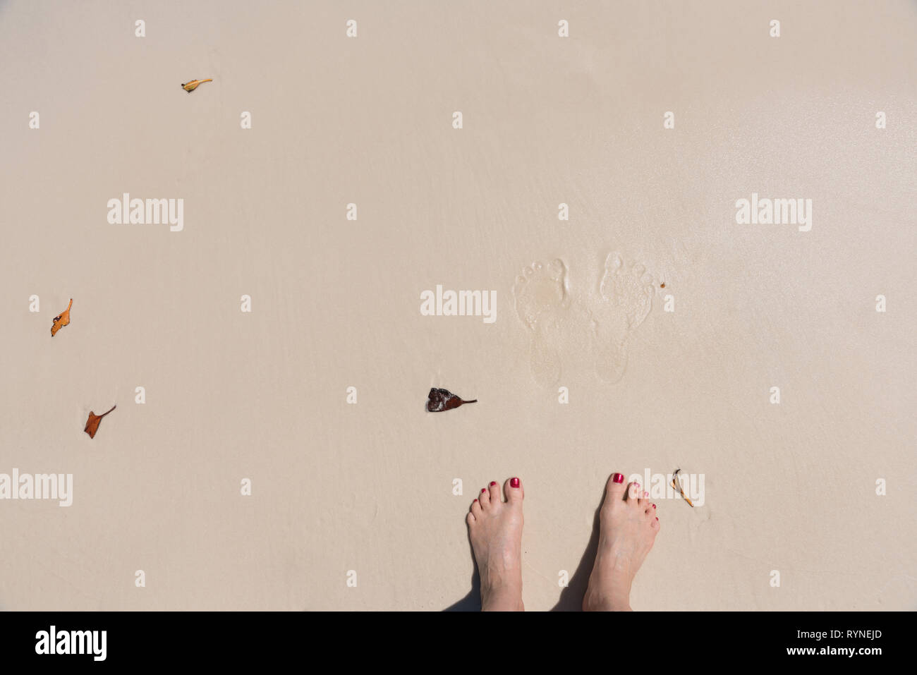 Footprint e piedi con dipinto toenails su sfondo di spiaggia Foto Stock