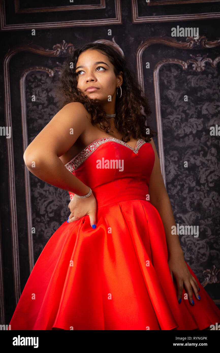 Una bella ragazza adolescente in rosso prom party dress guardando lontano con una mano sul fianco. Foto Stock