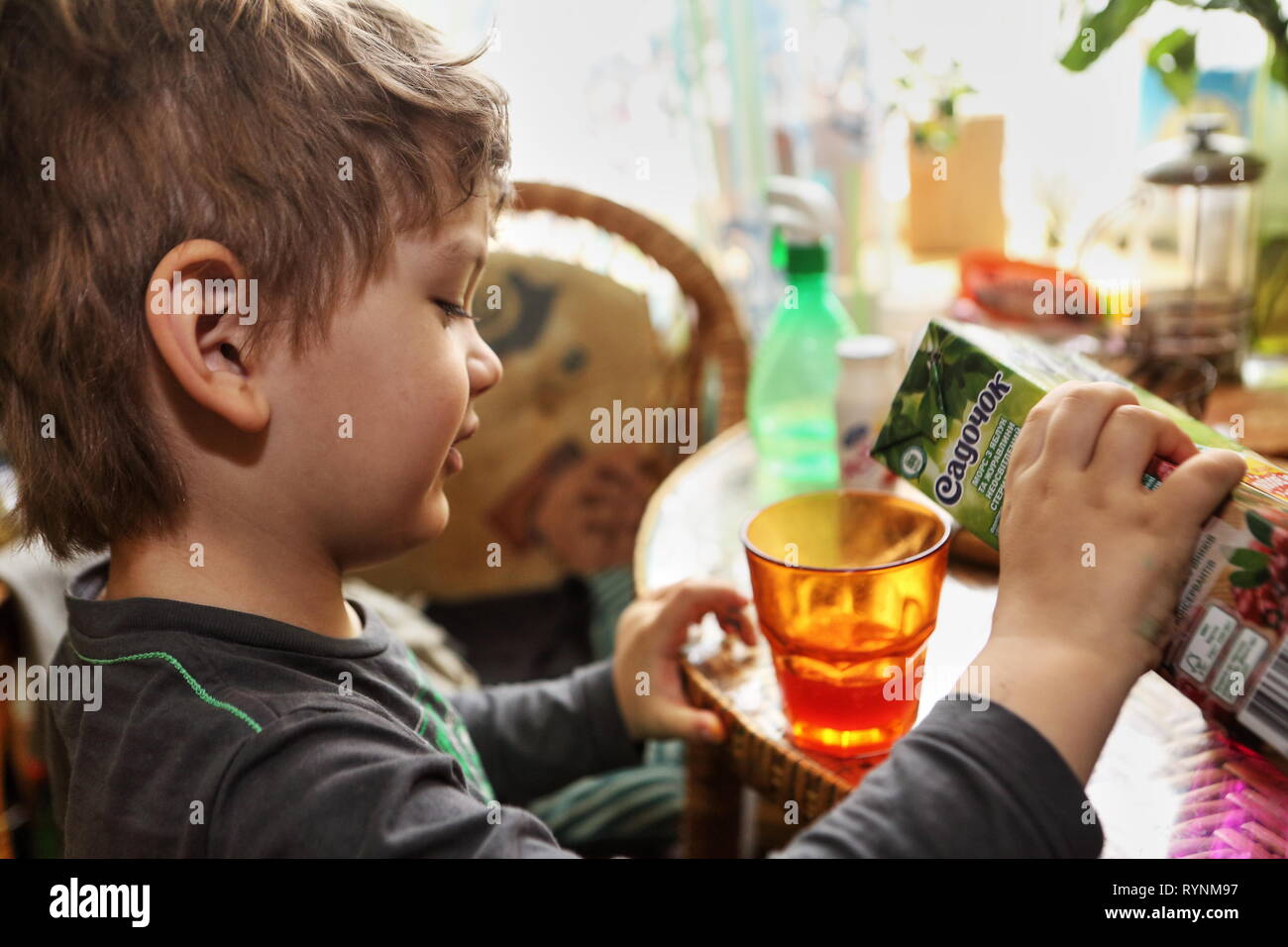 Little Boy riempie il vetro arancione con il succo di mirtillo palustre dal cartone seduti ad un tavolo durante una sana colazione come genitori insegnare a lui a essere un aiuto per te. Foto Stock