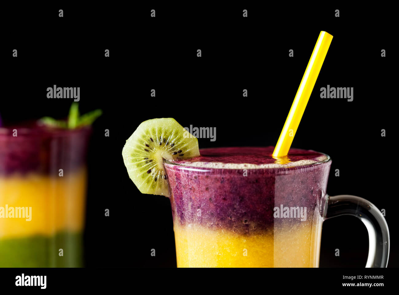 Due bicchiere di smoothie con strati colorati da kiwi, arance e blackberry su sfondo nero close up Foto Stock