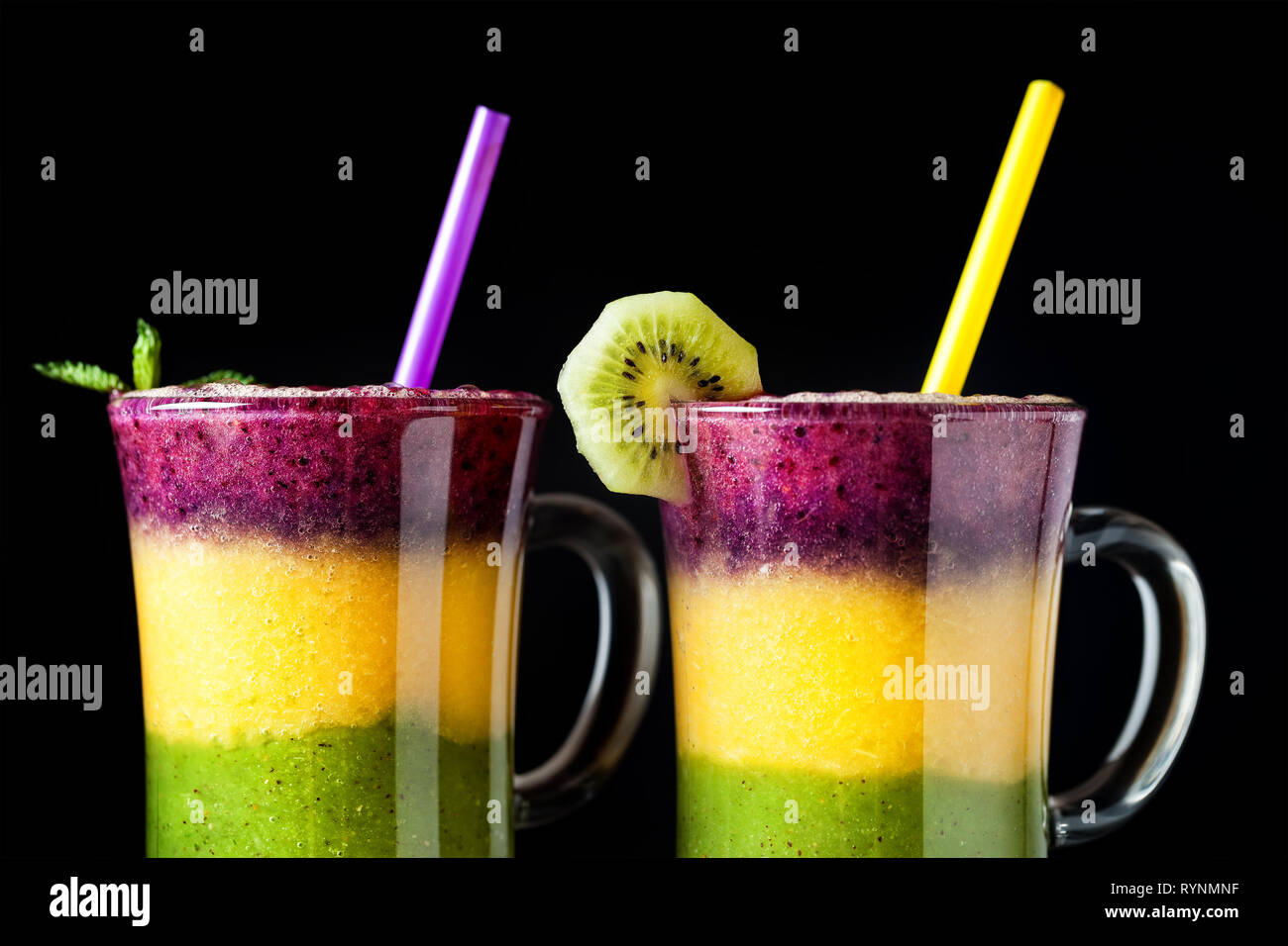 Due bicchiere di smoothie con strati colorati da kiwi, arance e blackberry su sfondo nero close up Foto Stock