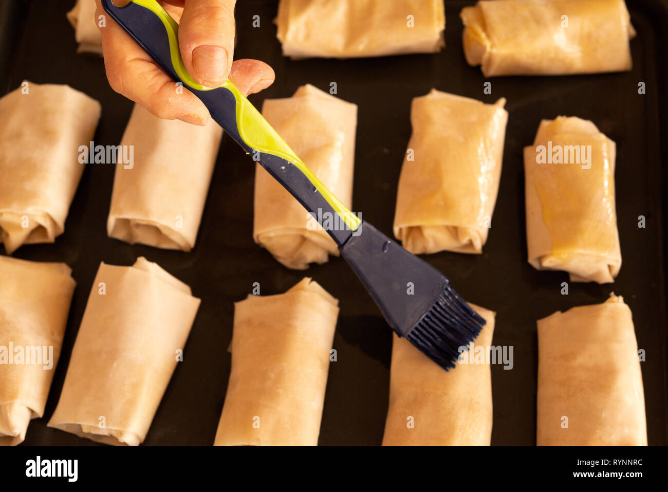 La mano della donna che applica il burro sul formaggio sfogliato morde il palloncino. Cuocere a mano lo chef in primo piano sfoglia sfogliate e bocconcini di formaggio. Foto Stock
