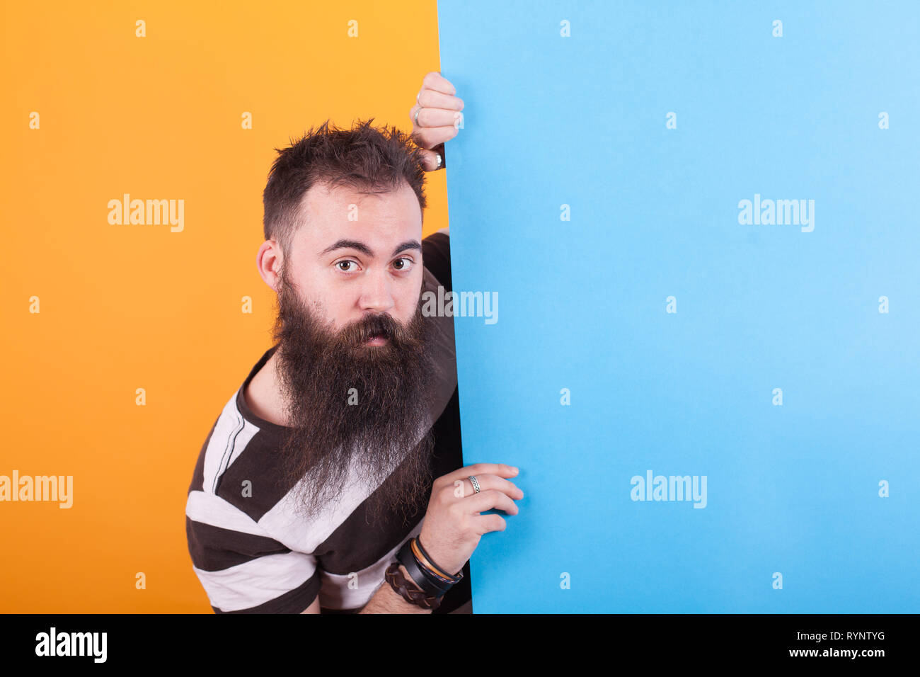 Attraente uomo con barba lunga in possesso di una copia blu spazio spogliato da indossare la t-shirt su sfondo giallo. Uomo bello. Elegante uomo. Gli uomini lo stile. Foto Stock