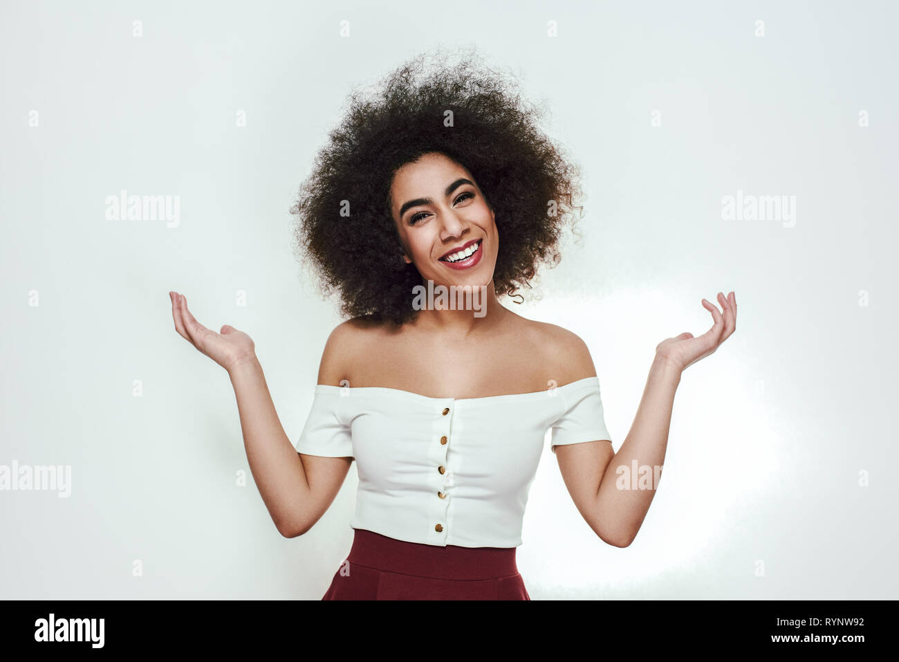 Non so, mi spiace! Ritratto di bello e attraente afro american donna che guarda con fotocamera e sorridente, diffondendo le mani e piedi contro uno sfondo grigio. Concetto di dubbio. Donne bellezza. Ritratto in studio Foto Stock