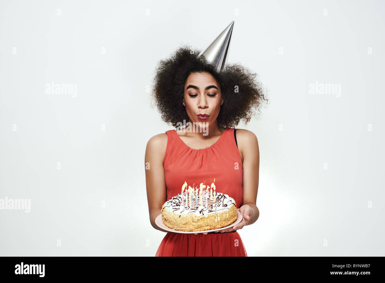 Piuttosto giovani afro american donna in argento party hat festeggia il suo compleanno e soffiando le candeline sulla torta deliziosa. Celebrazione del concetto. Il concetto di partito Foto Stock