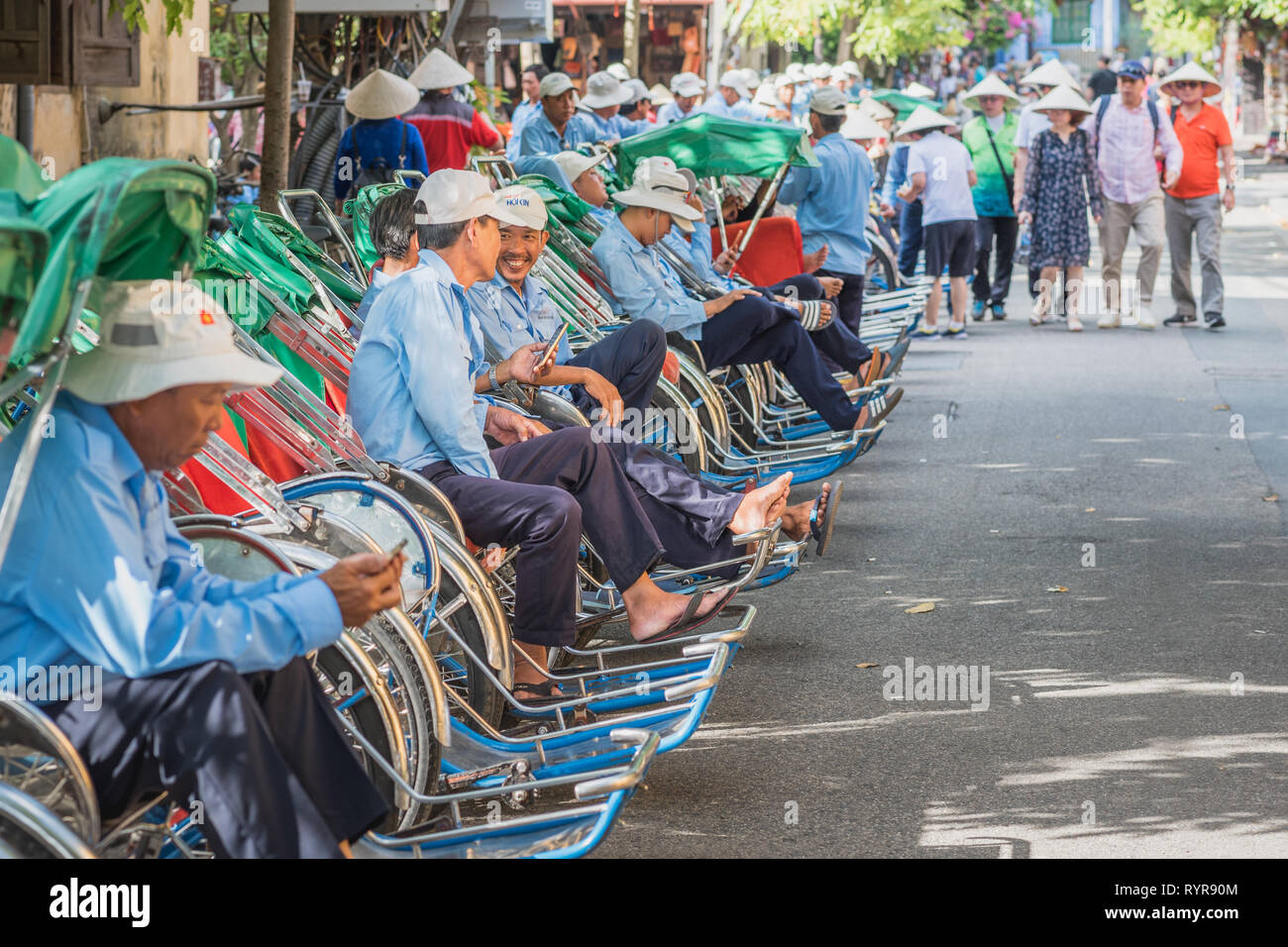 Hoi An, Vietnam - Ottobre 23, 2018: una lunga fila di trishaws divise in attesa per i clienti, un avvicinamento gruppo di turisti in cappelli conici. Foto Stock