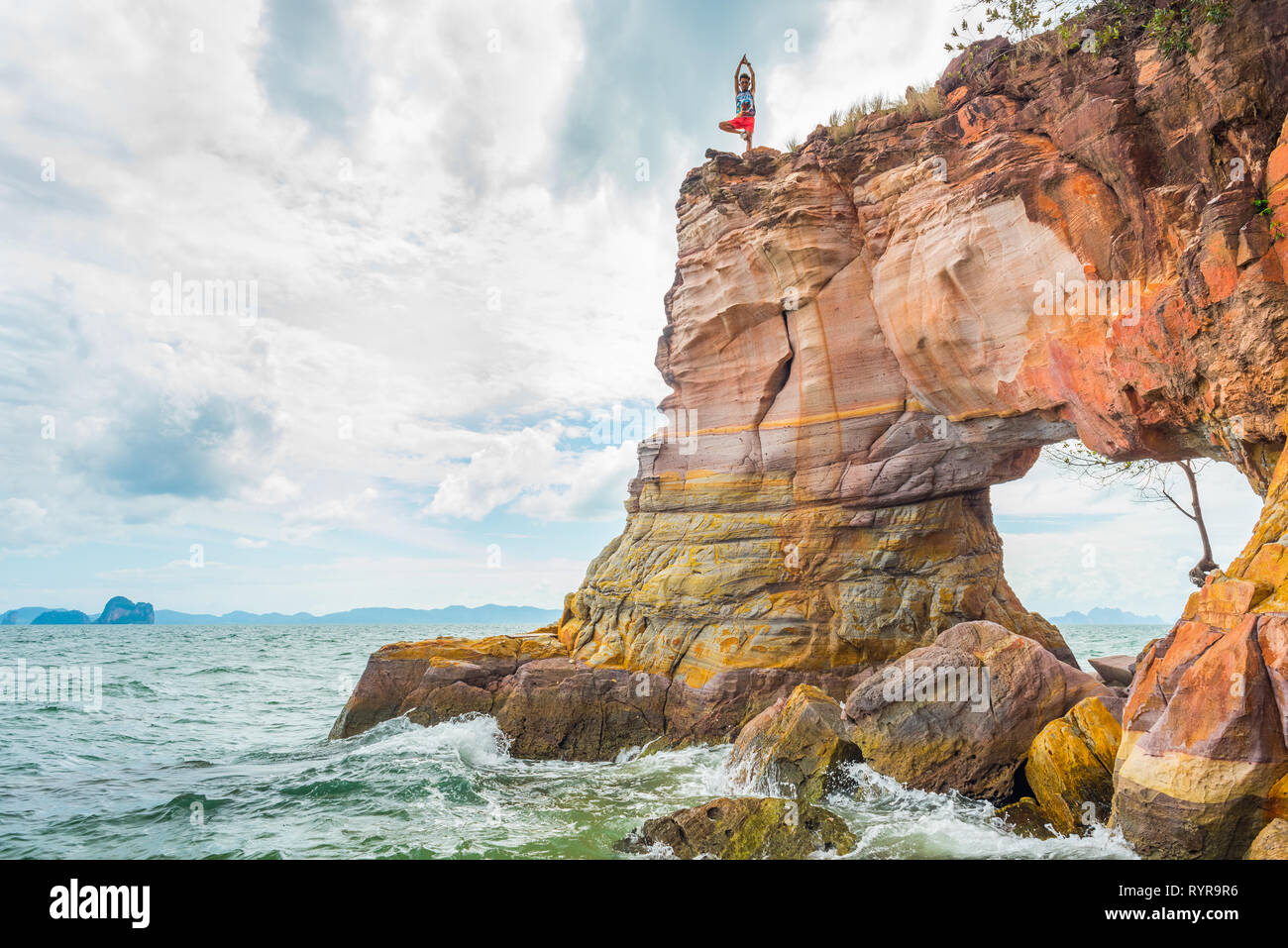 Arch Rock in mare con un giovane uomo in piedi su una gamba sola sulla sua sommità. Un concetto di yoga, fitness e uno stile di vita sano. Krabi, Thailandia. Foto Stock